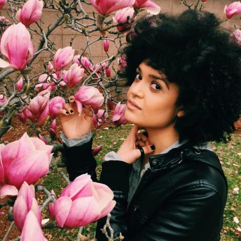 Headshot of Diannely Antigua, posing next to a tree in bloom.