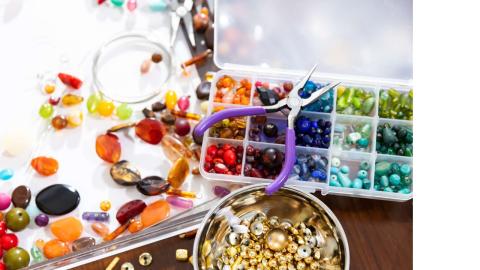 An array of supplies for jewelry making, including various colored and styled beads, as well as needle-nose pliers.