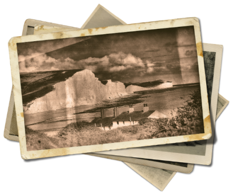 A loose stack of old photographs, the top one depicting a seaside cliff. They are all sepia-toned, stained, and a little wrinkled.