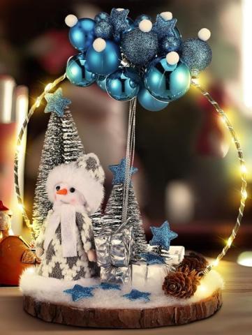 Photo of a wintery ornamental tabletop craft, with a small snowman, some trees, and presents, under a ring decked out with blue bauble ornaments.