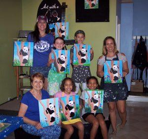 Group of teens displaying paintings of pandas made at an Art with a Splash event.