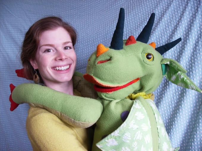 Image of performer Lindsay, holding a large green dragon puppet.