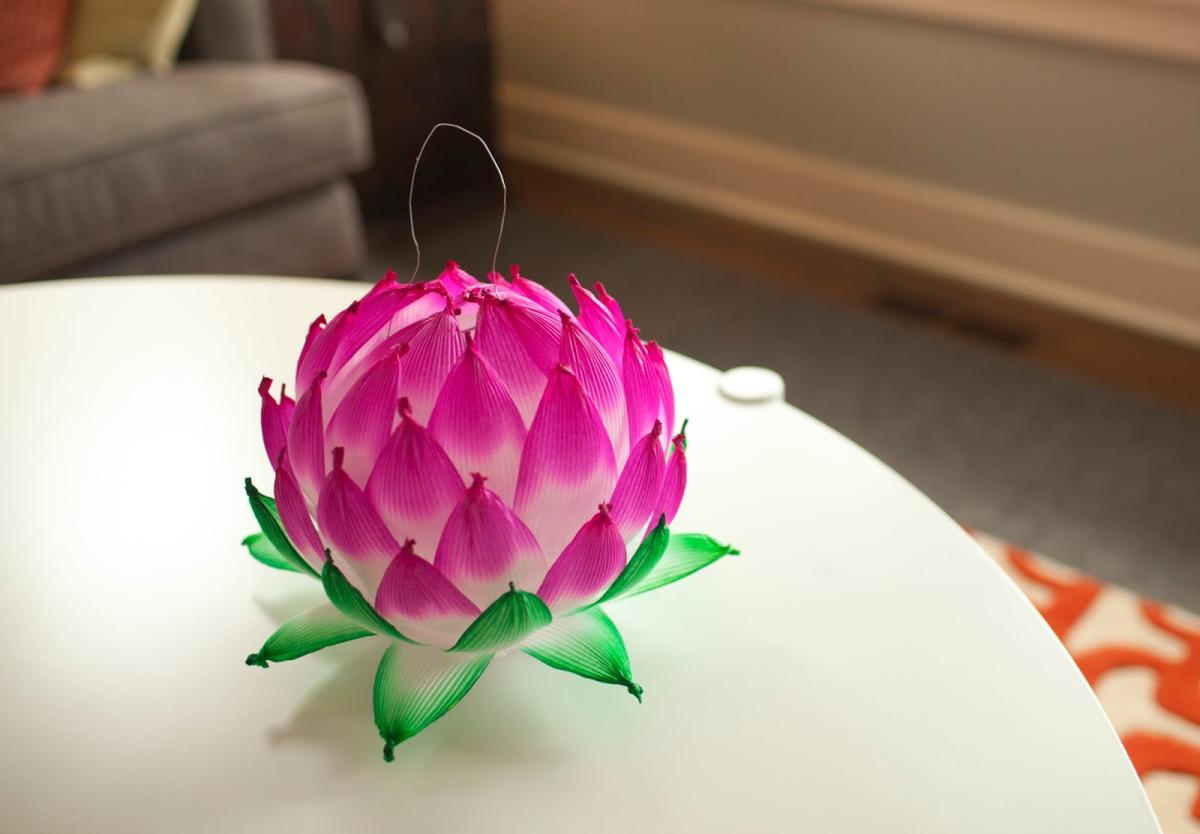 Pink and white paper lantern in the shape of a lotus flower sits on a white side table.